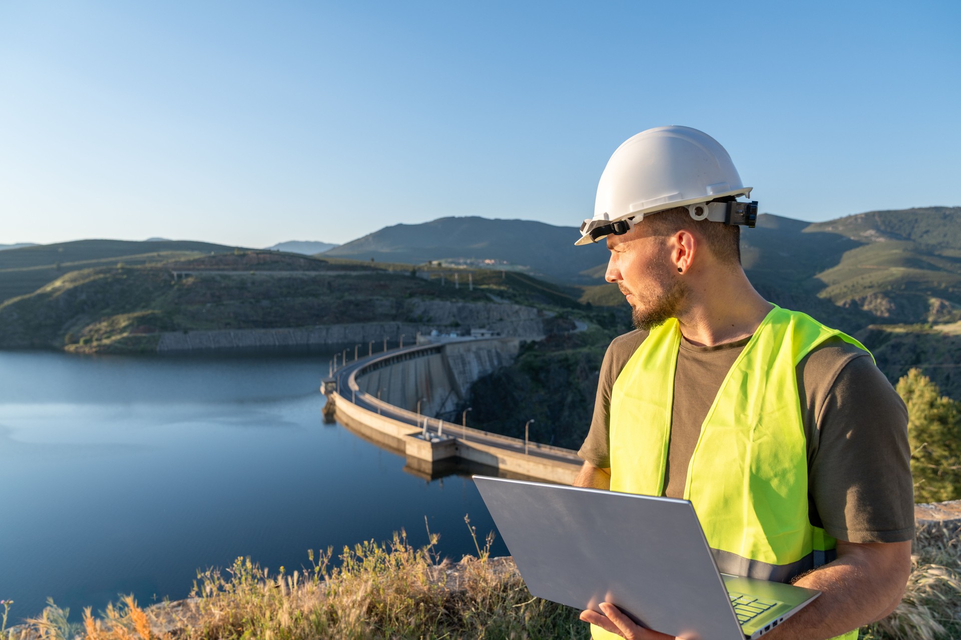 Engineer inspecting a reservoir dam with laptop